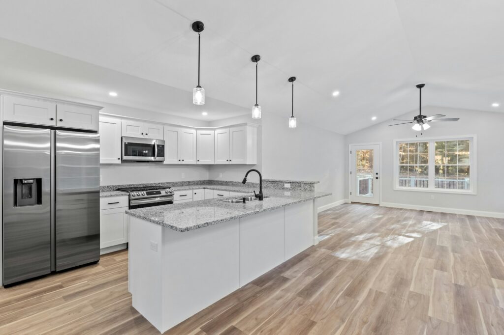Newly renovated kitchen with hardwood floors, white furniture, silver appliances and a marble island